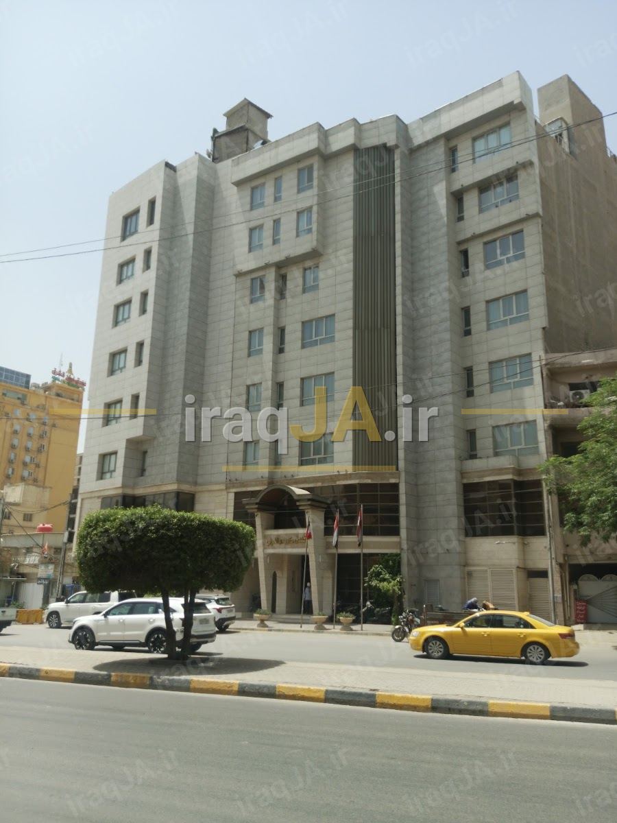 ساختمان چندطبقهٔ سنگی هتل در روز، کنار خیابان با تاکسی زرد